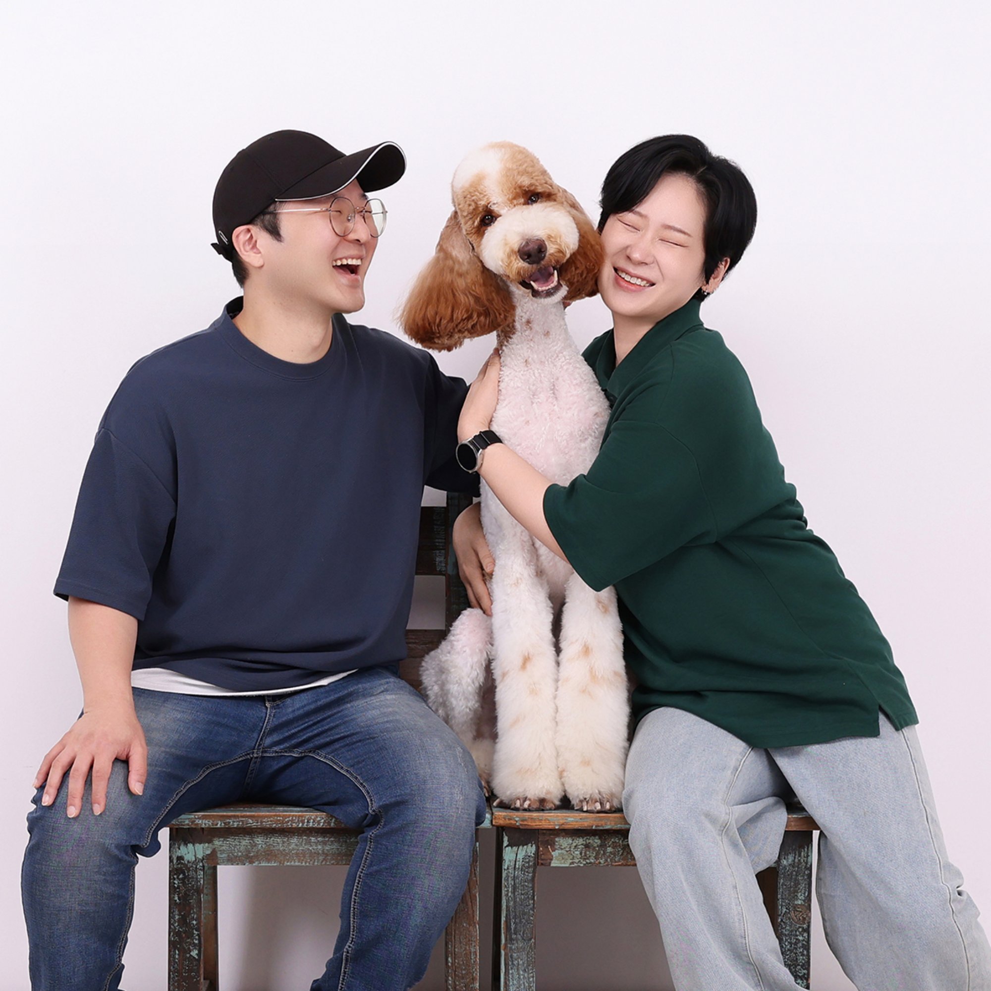 의자에 앉아 갈색·흰색 곱슬 대형견을 끌어안고 웃는 두 사람의 개족사진