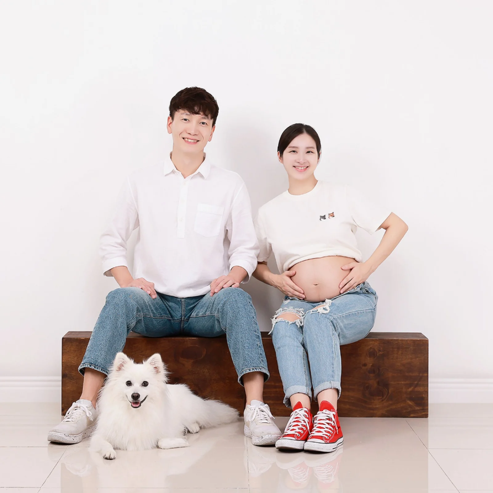 나무 상자에 앉아 배에 손을 얹은 사람과 옆 사람, 앞에 엎드린 흰 장모견의 개족사진