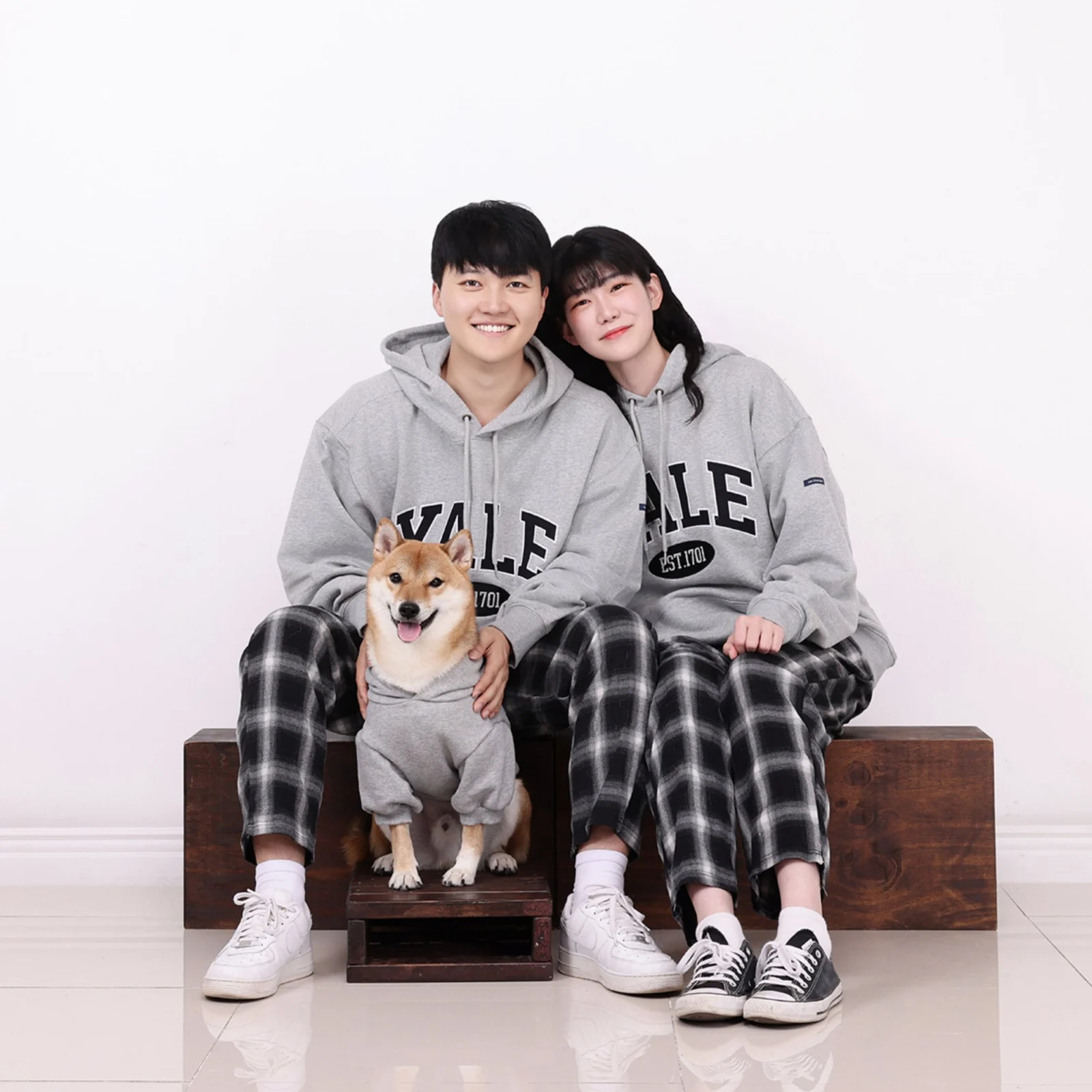 나무 상자에 앉은 회색 후드 두 사람 앞 받침에 옷 입은 갈색 개가 앉은 정사각 개족사진
