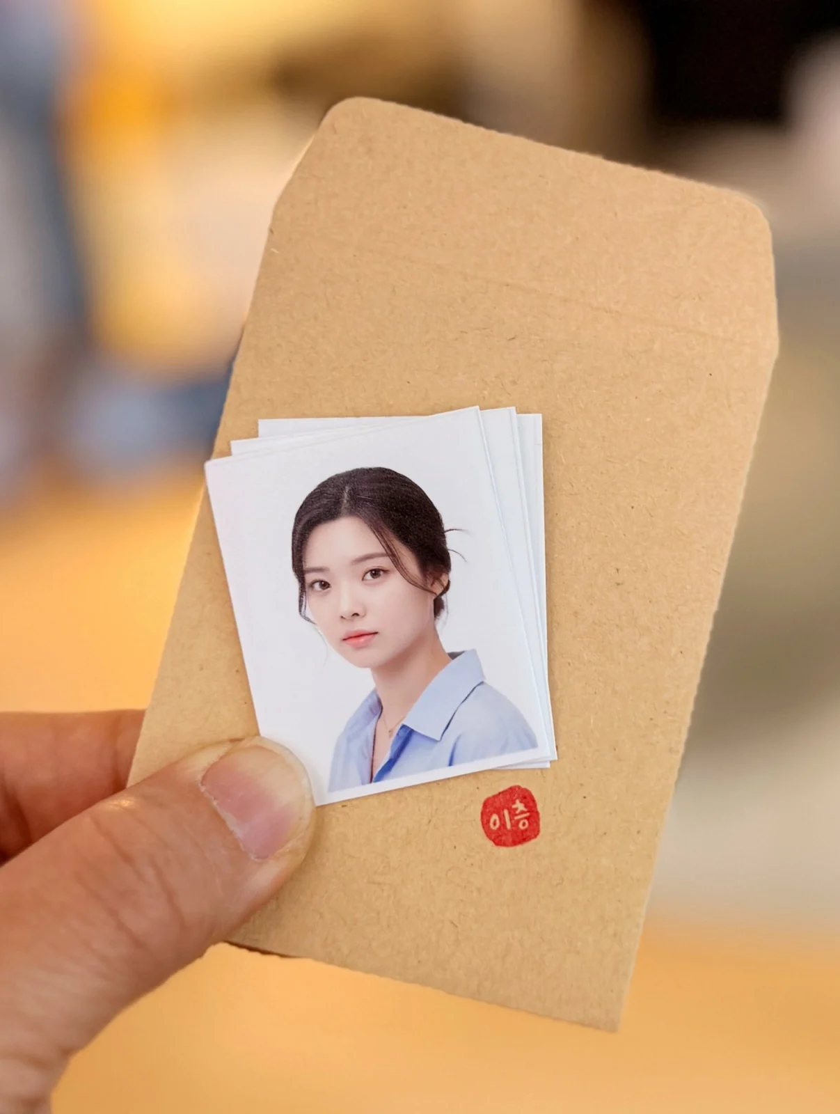 하늘색 셔츠 차림 증명사진 인화본 여러 장을 봉투와 함께 손에 든 모습