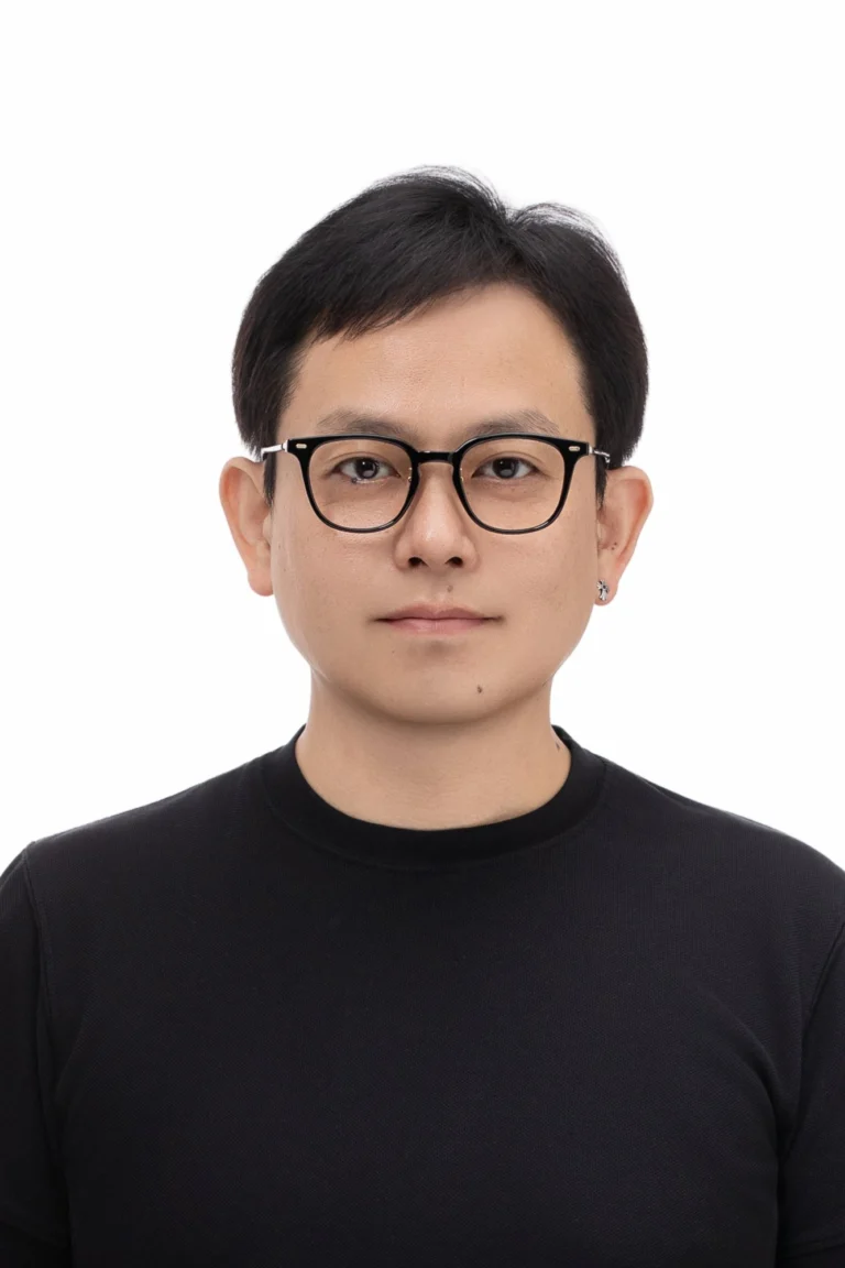 흰 배경에서 검정 뿔테 안경을 쓰고 검정 니트를 입은 증명사진