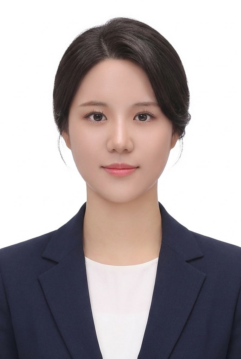 머리를 뒤로 넘겨 묶고 남색 재킷과 흰 상의를 입은 인물의 흰 배경 증명사진